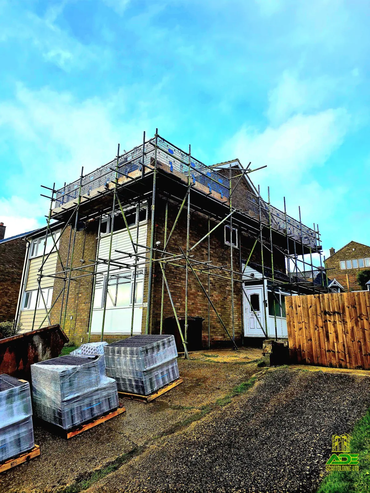 Wraparound scaffold on a semi-detached house with a dormer and a pallet of blocks